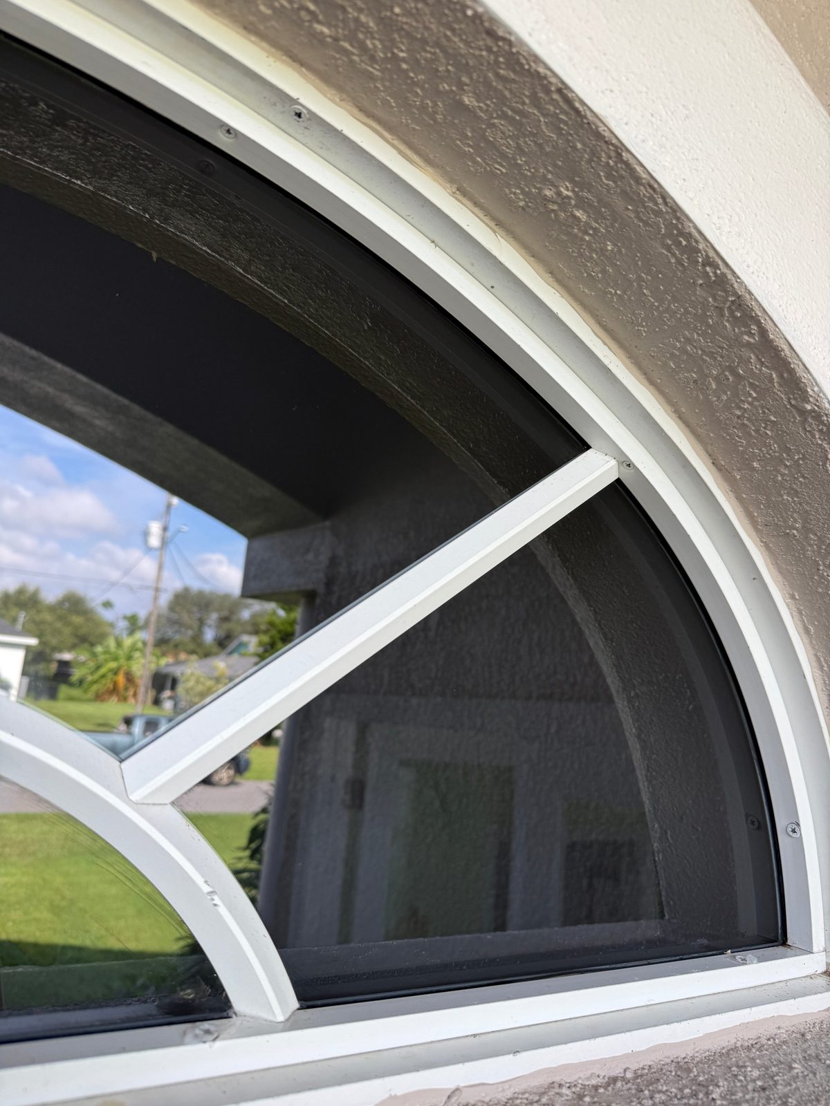The same corner of the arched window after cleaning, with clear glass and a clean white grille bar, frame and sill